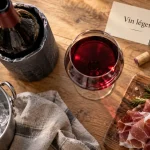 Vin rouge léger en verre rubis, bouteille rouge léger et seau à glace sur table bois clair